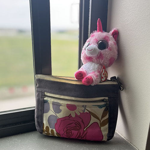 Purple and floral purse next to a window with a unicorn sticking out of the purse